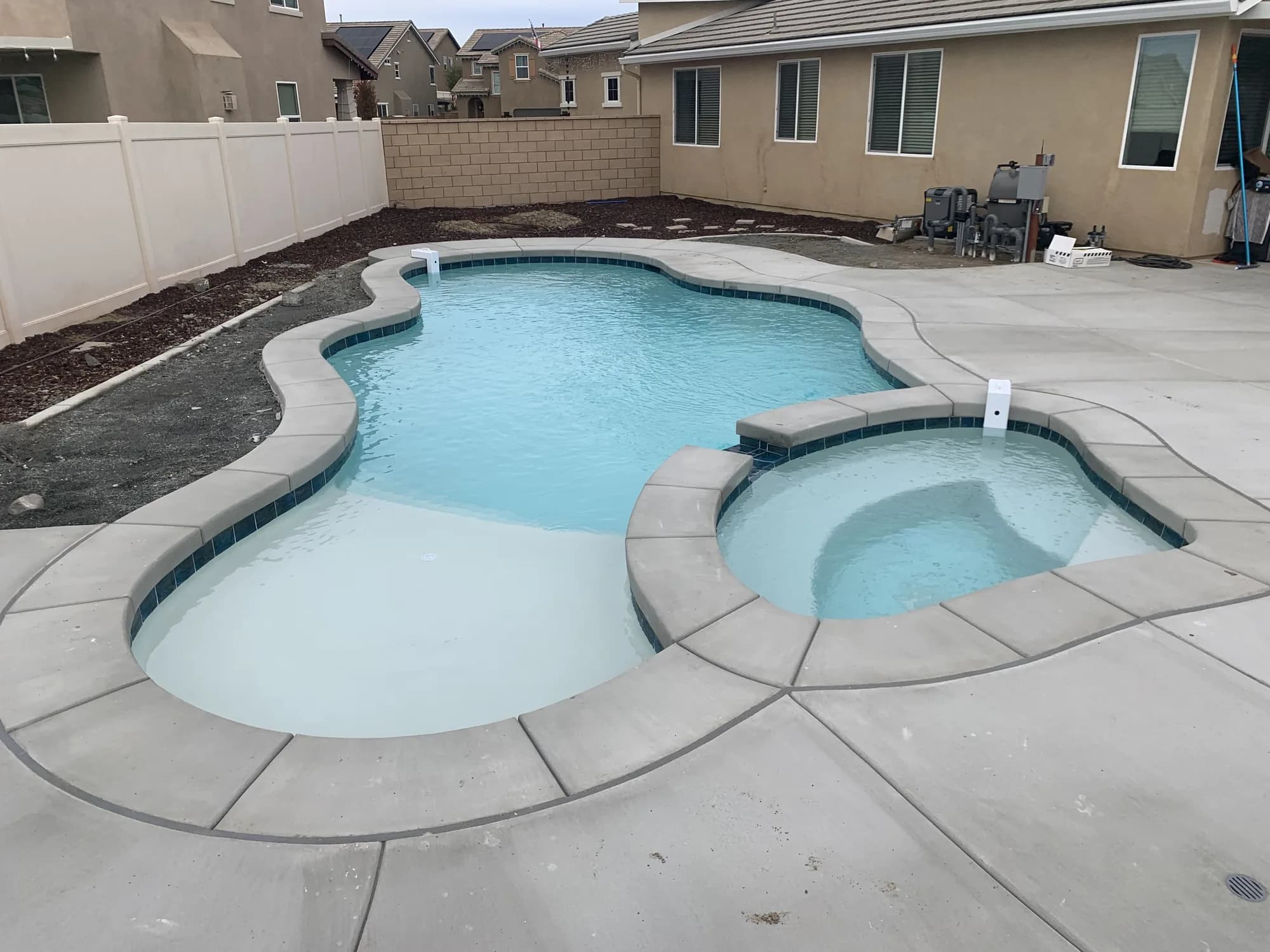 Freeform pool with a shallow ledge and an attached round spa on a concrete deck