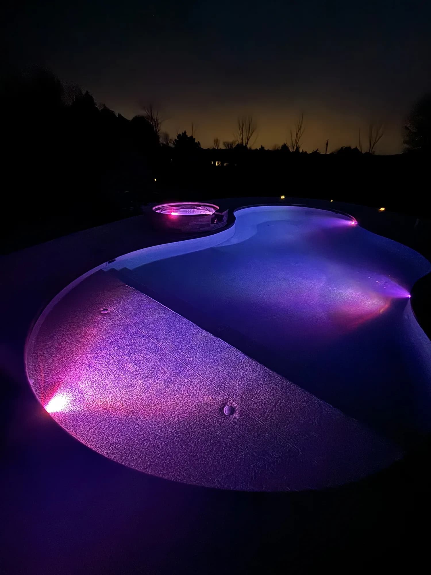 Freeform pool glowing purple and blue beneath a dark evening sky