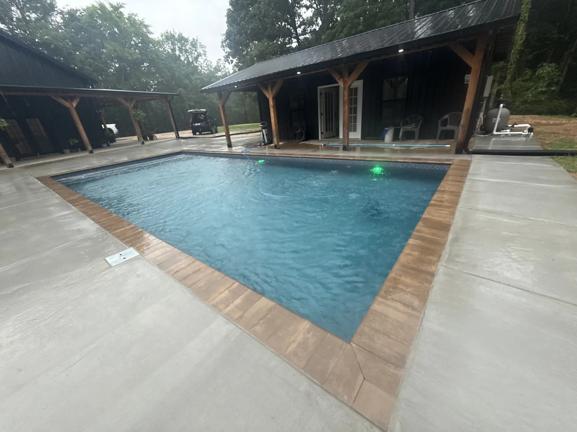 Rectangular pool framed by light concrete decking and a large covered backyard pavilion