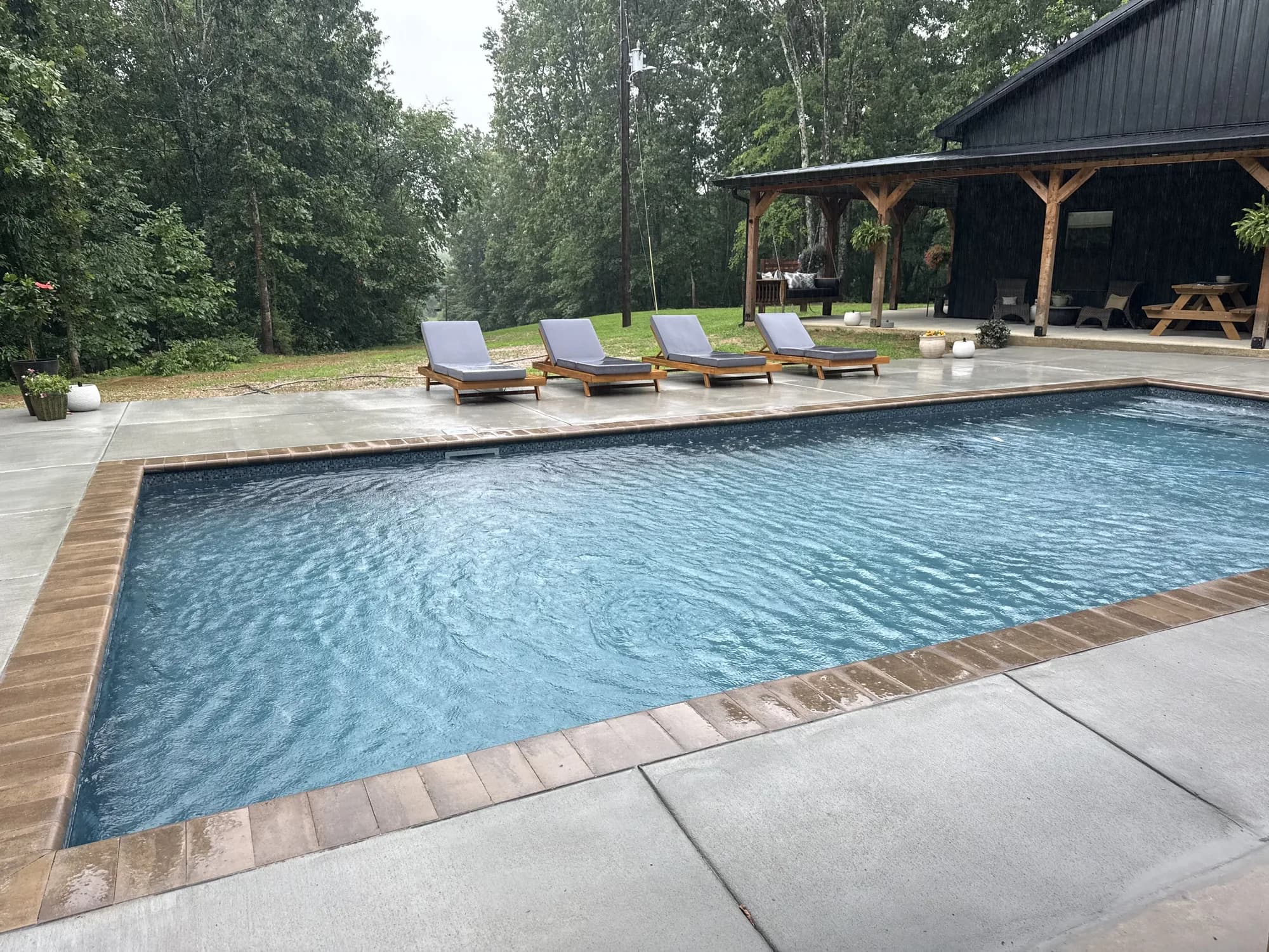 Rectangular pool with wood-look coping, chaise lounges, and a covered timber pavilion
